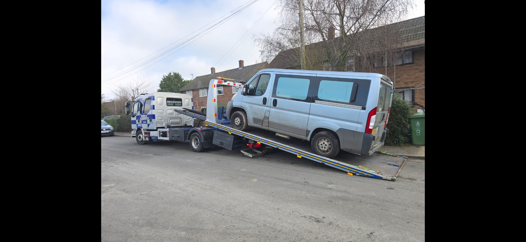 Recovery truck transporting a blue car on a town road